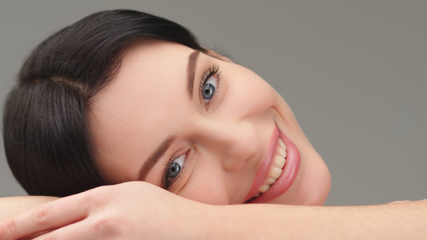 美丽的年轻模特把头靠在手上，躺着看着镜头。以健康肌肤和女性美容为理念，服务美容。图片下载