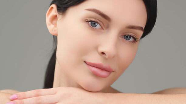 美丽的年轻模特把头靠在手上，躺着看着镜头。以健康肌肤和女性美容为理念，服务美容。图片下载