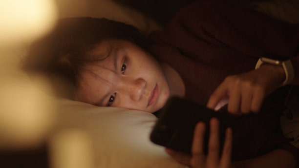 女孩晚上在床上玩智能手机。图片下载