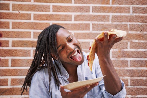 一个年轻人在街上吃着一片披萨。图片下载