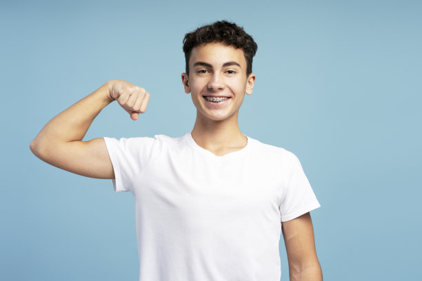 照片中微笑的强壮的十几岁男孩穿着时尚的白色t恤，露出肌肉看着镜头图片下载