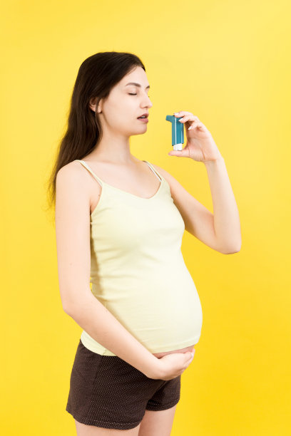 孕妇手持哮喘病吸入器，以防止攻击在彩色背景与复制空间。未来的母亲患有呼吸系统疾病。哮喘的概念图片下载