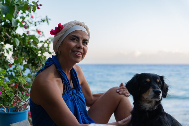 夏天，克里特岛南部，一名女子坐在一家希腊酒馆里，头上戴着一件花衣服，与当地吉祥物一起享受日落时分的放松时光图片下载