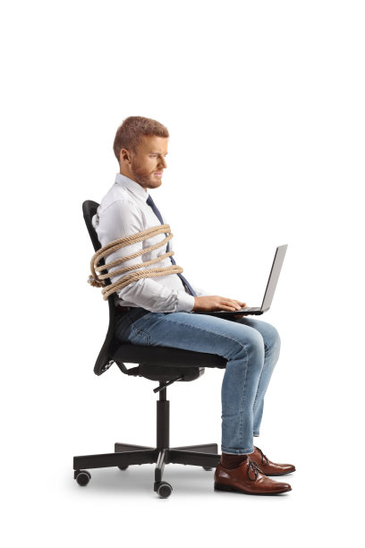 一名男性办公室职员的侧面照片，他坐在椅子上，用绳子绑着，用笔记本电脑工作图片下载