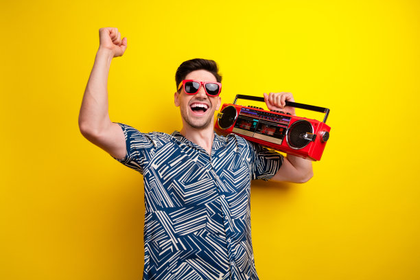 喜出望外的积极的人举着拳头跳舞的照片在黄色的背景上孤立地携带着音箱图片下载