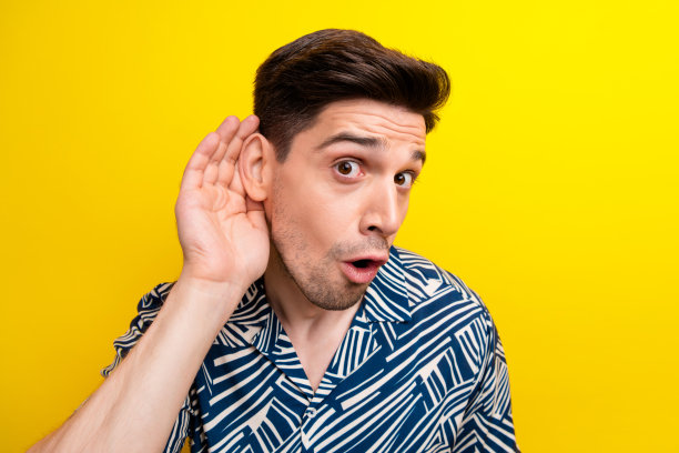 困惑震惊的年轻男子张开嘴，手臂靠近耳朵偷听的照片被隔离在黄色背景上图片下载