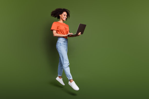 可爱的正面女子全身照片穿着橙色t恤跳跃工作的现代装置空白空间孤立的绿色背景图片下载