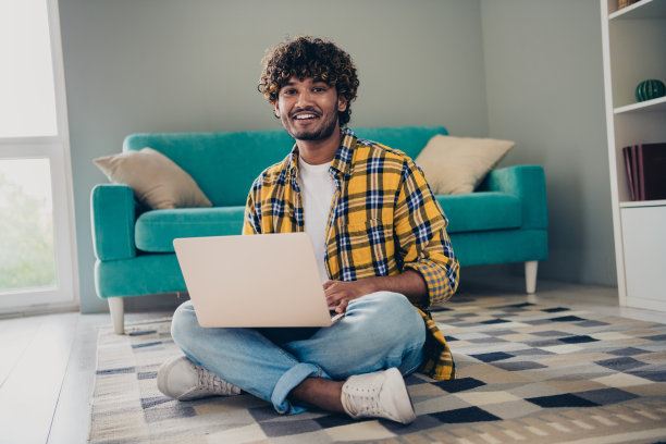 愉快的好男人学生穿着衬衫坐在室内地毯上使用现代上网本设备的照片从国内学院大学教育图片下载