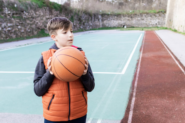 一个男孩在体育场上拿着篮球的照片。图片下载