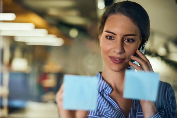 一个美女在玻璃墙上贴便利贴打电话的特写照片。图片下载