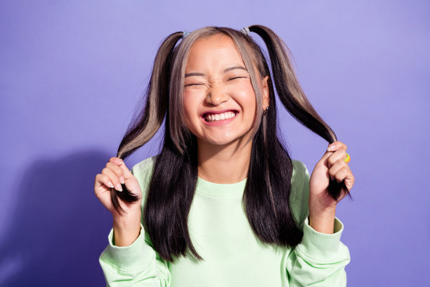 照片中时髦的女人穿着绿色的运动衫，染了色的发型，把自己的马尾辫孤立在紫色的背景上图片下载