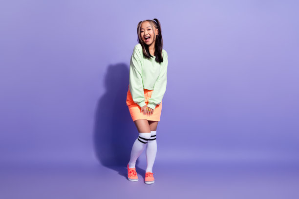 可爱漂亮的日本女人的全身照片，染了色的发型，穿着绿色的运动衫长袜，孤立在紫色的背景上图片下载