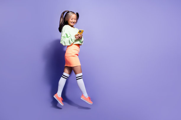 全身尺寸的照片的青年黑发尾发女孩跳空气浏览智能手机爱有乐趣孤立在紫色的背景图片下载