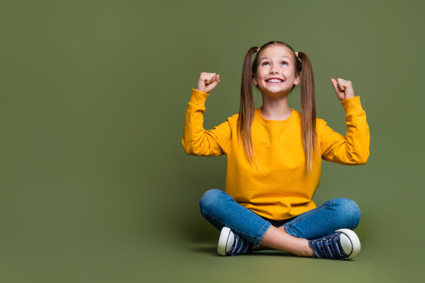 满意的女学生的全尺寸照片，扎着马尾辫，穿着黄色套头衫，抬头看着卡其色背景上孤立的空白图片下载
