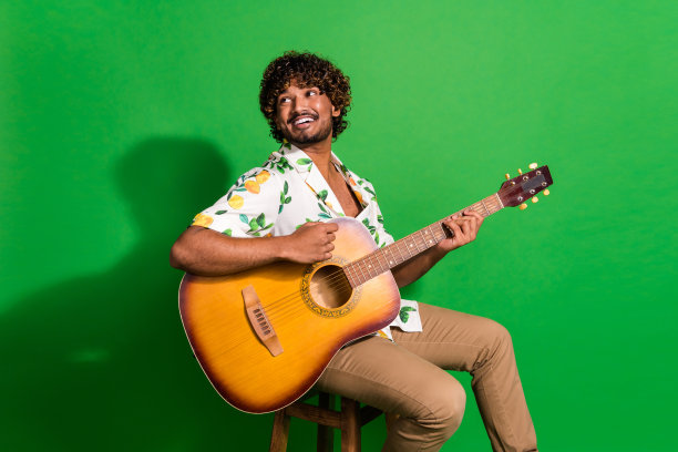 有吸引力的年轻人的照片坐在椅子上看空空间吉他手穿着时尚的柑橘印花衣服孤立的绿色背景图片下载