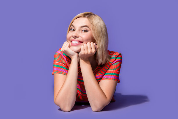 照片的漂亮少女年轻漂亮的女人触摸脸颊在条纹t恤愉快的微笑模型孤立在紫罗兰色背景图片下载