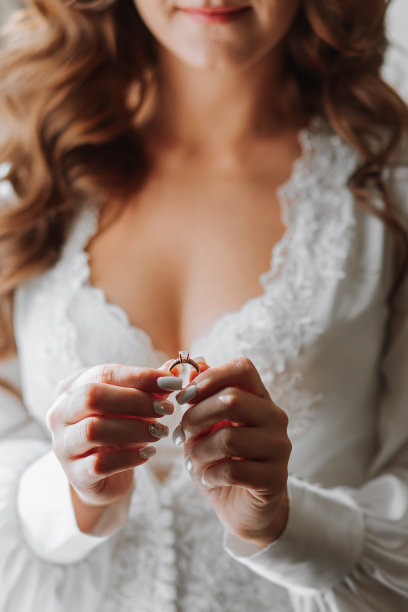 一个穿着白色开裙的卷发女孩手里拿着一枚镶着宝石的结婚戒指。特写照片图片下载