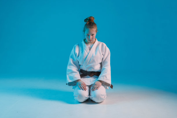 女孩柔道在白色和服与黑腰带在蓝色背景，工作室照片图片下载
