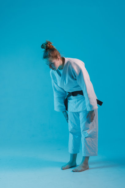 女孩柔道在白色和服与黑腰带在蓝色背景，工作室照片图片下载