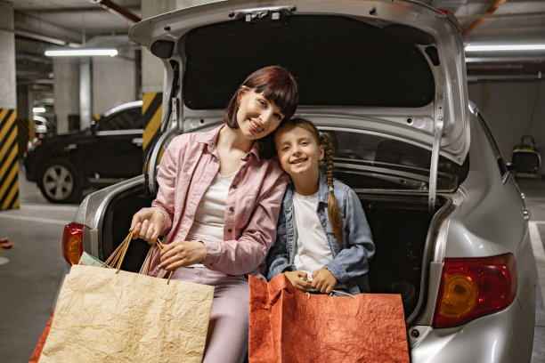 白人母亲和小女儿坐在现代汽车打开的后备箱上。图片下载