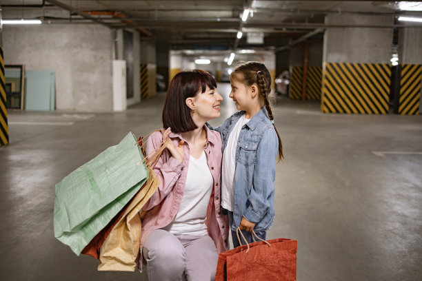 快乐的女人抱着小孩，手里拿着装着衣服的彩色袋子。图片下载