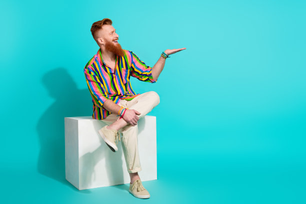 红头发的全身照片，男子潮人坐在讲台上，抱着手臂，新的香水广告孤立在青色背景图片下载