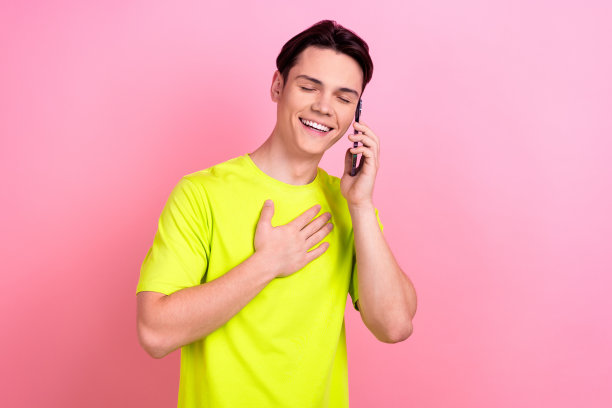 照片肖像英俊的青少年男子讲电话笑着穿着时髦的黄色服装孤立在粉红色的背景图片下载
