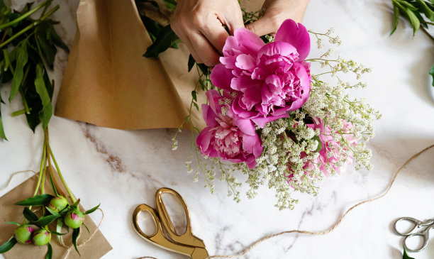 一位女花店老板在桌面上用牛皮纸包着一束牡丹花。从上面看。高质量照片图片下载