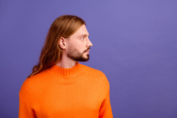 侧照片的金发男子穿橙色套头衫看起来新奇促进发型师理发店孤立的紫色背景图片下载