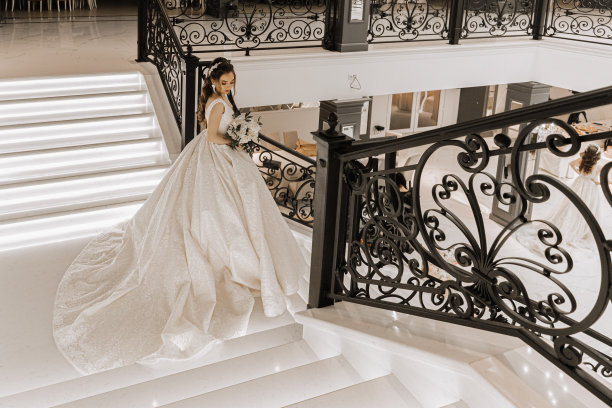迷人的工作室照片，一个女孩穿着婚纱，拖着长长的拖尾，手里拿着一束玫瑰，站在楼梯上。豪华的内饰。广角照片。图片下载