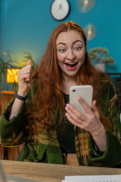 女人在家里用智能手机庆祝成功，胜利，玩网络游戏，好消息图片下载