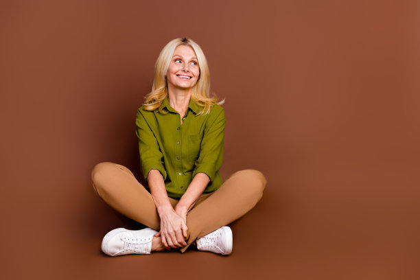 心情好的人穿着卡其布衣服的全身照片，坐在地板上看广告，在深棕色背景上孤立的空白空间图片下载