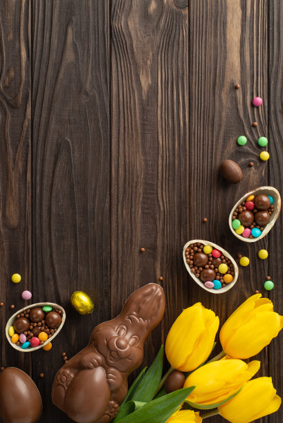 节日复活节糖果展示:俯视图垂直照片，巧克力蛋被打开，充满活力的糖果，巧克力兔子，郁金香放在木桌上，有文字或广告的空间图片下载