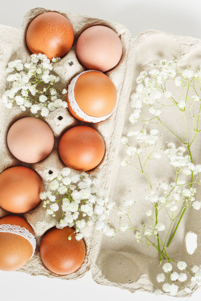 棕色复活节彩蛋装饰花边和白色的吉思非亚花在纸盒在白色的背景。复活节庆祝概念。俯视图照片与节日食品有机彩绘鸡蛋图片下载