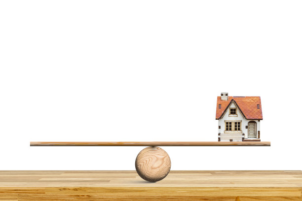 有红色屋顶的白宫。房子坐落在一个木制跷跷板上，跷跷板在一张木桌上保持平衡。图片下载
