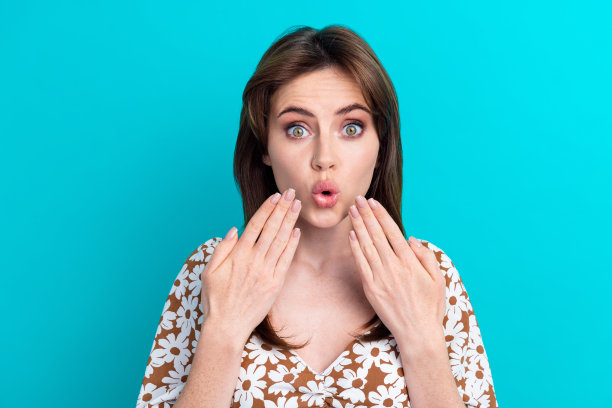 漂亮的年轻女子的特写照片，黑发，触摸脸颊，惊讶丰满的嘴唇，无言以对孤立的海蓝宝石色背景图片下载