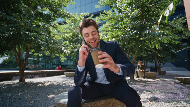 在城市公园里喝咖啡的快乐男人打来电话。微笑交谈的商人图片下载