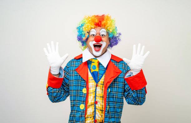 小丑先生。滑稽的震惊脸喜剧演员小丑的肖像，穿着五颜六色的服装，戴着假发，站着摆姿势，对着镜头微笑。在孤立的背景下，快乐的表情让人惊讶。图片下载