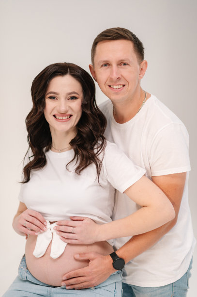 怀孕的女人和男人把袜子放在肚子上，放在家里未来女儿或儿子的肚子上。等待孩子的夫妇。怀孕夫妇抱着肚子。家庭隔离在白色背景上。图片下载