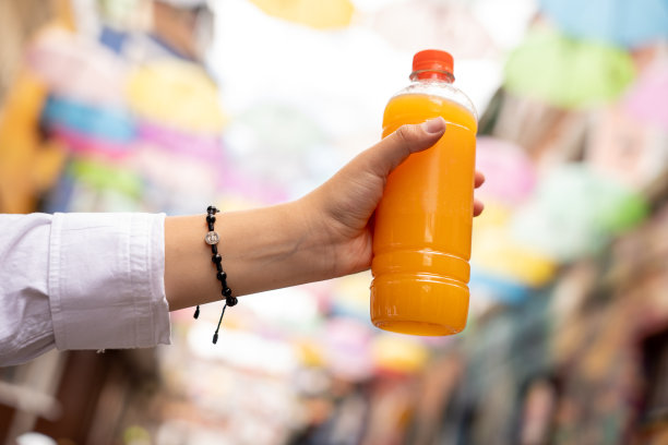塑料瓶里装着橙汁，背景是城市和五颜六色的雨伞图片下载