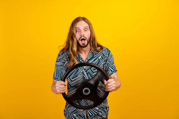 照片兴奋时髦的男人穿着印花衬衫驾驶汽车张开嘴孤立的黄色背景图片下载