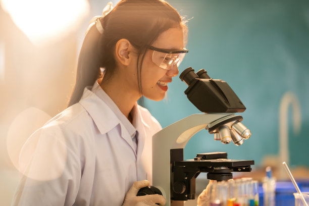 在温暖的光线下用显微镜拍摄的在科学实验室工作的女医生的肖像，带有美丽的散景。生产药品和疫苗，分发给世界各地的医生和医院。图片下载