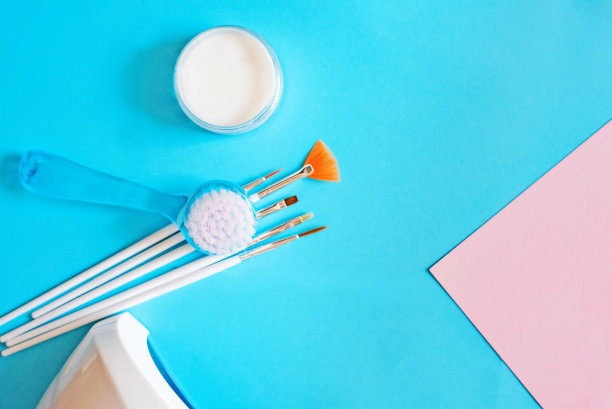 在蓝粉色的背景上，一组指甲刷和一盏LED灯。指甲设计用粗粉。为美容院，指甲设计工作室。图片下载