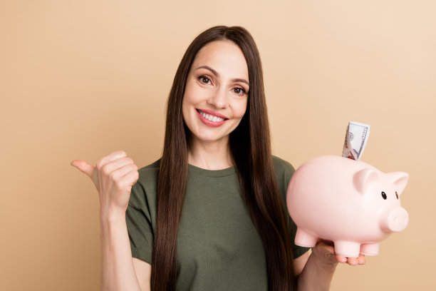 照片上的百万富翁女人穿着卡其色t恤存钱，把它们放在米色的背景上，用手指指着空的地方图片下载