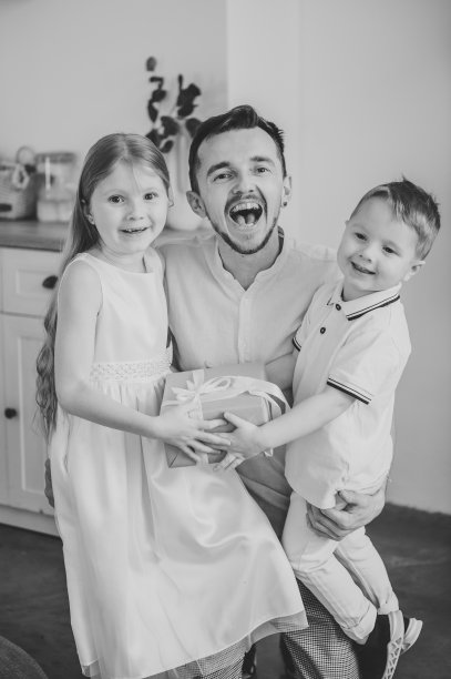 孩子拥抱和问候快乐的父亲特写。女儿微笑着给爸爸送礼盒礼物。孩子们祝贺爸爸。儿子为父亲节带来惊喜。看着镜头。黑白照片图片下载