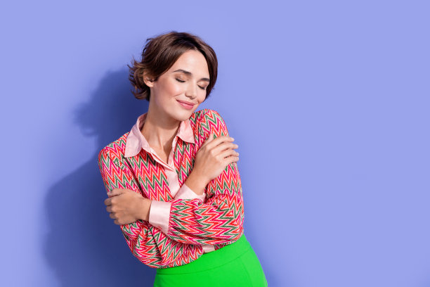 照片肖像迷人的年轻女子闭上眼睛拥抱自己享受香气穿着时尚的印花衣服孤立在紫色的背景图片下载