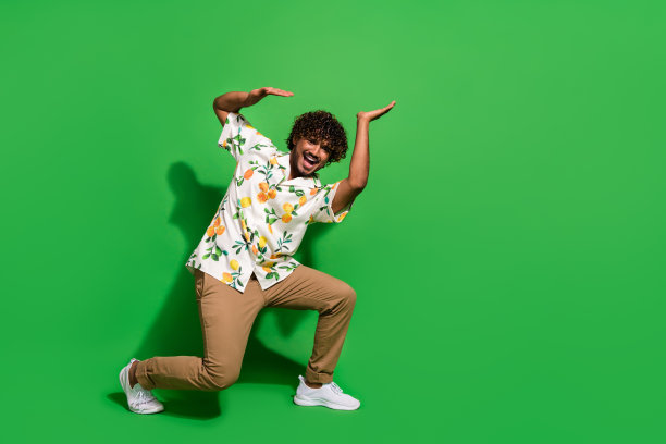 英俊的年轻人的全身照片推沉重的空白空间穿时髦的柑橘印花服装孤立的绿色背景图片下载