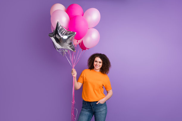 照片心情好可爱的女人穿着橙色t恤拿着大气球花束孤立的紫色背景图片下载