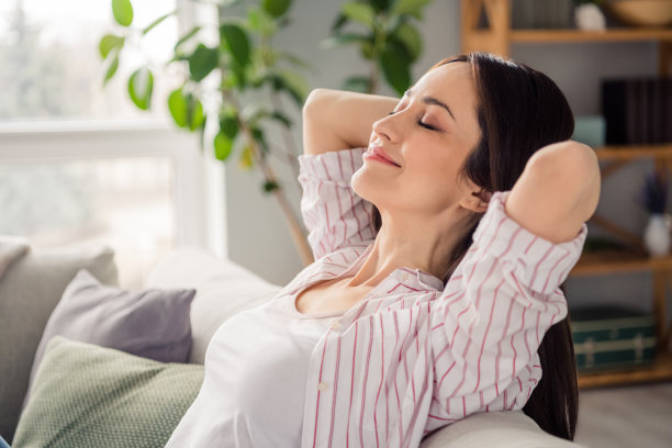 华丽甜美女士的个人资料照片坐在舒适的沙发上，闭上眼睛，手在头后面明亮的公寓室内图片下载