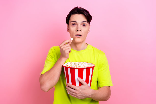 漂亮的青少年男子的照片肖像吃爆米花看惊悚片害怕穿着时髦的黄色衣服孤立在粉红色的背景图片下载